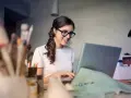 Uśmiechnięta kobieta w okularach pracuje przy laptopie, realizując swoją pracę dodatkową z domu.