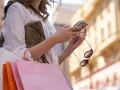 Kobieta z zakupami sprawdza telefon, planując refinansowanie pożyczki.