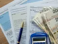 Formularze podatkowe PIT, długopis i stos banknotów 200 zł. Dokumenty sugerują rozliczenie dochodu zwolnionego od podatku.