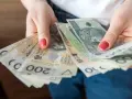 Dłonie trzymają stos banknotów 100 i 200 zł. To może być kwota wolna od podatku 60000 zł, która pozwala na swobodne planowanie wydatków.
