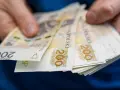 Dłonie trzymają stos banknotów 200 zł. To symbol oszczędności Polaków, które budują bezpieczeństwo finansowe.