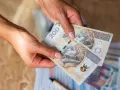 Dłonie trzymają banknoty 200 zł. Czy na lokatę można wpłacać pieniądze co miesiąc?