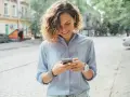 Uśmiechnięta kobieta na ulicy sprawdza telefon, być może szuka informacji o pożyczka kontomatik.