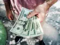 Dłoń trzyma kilka banknotów po 20 dolarów, symbolizując sposób, jak zarabiać więcej.