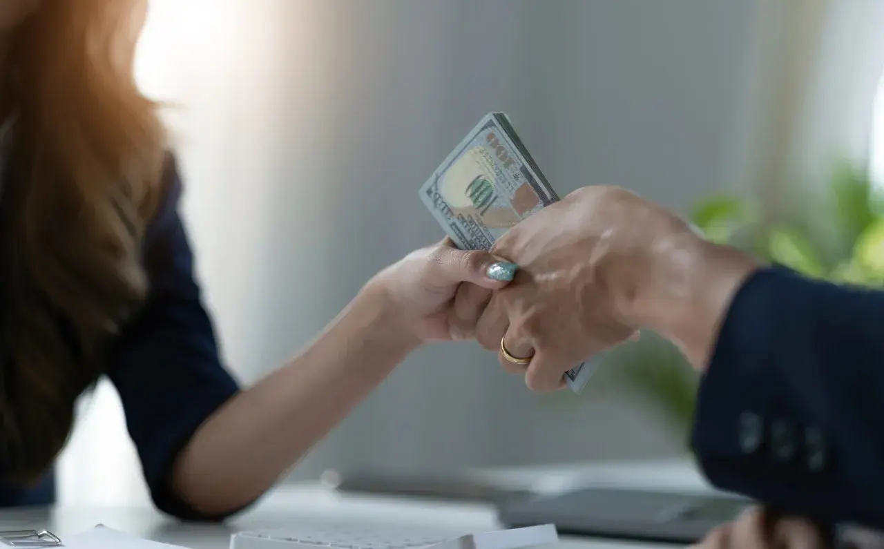 Dwie osoby przekazują sobie plik banknotów. To może być początek prywatnej pożyczki, która pomoże zrealizować marzenia.