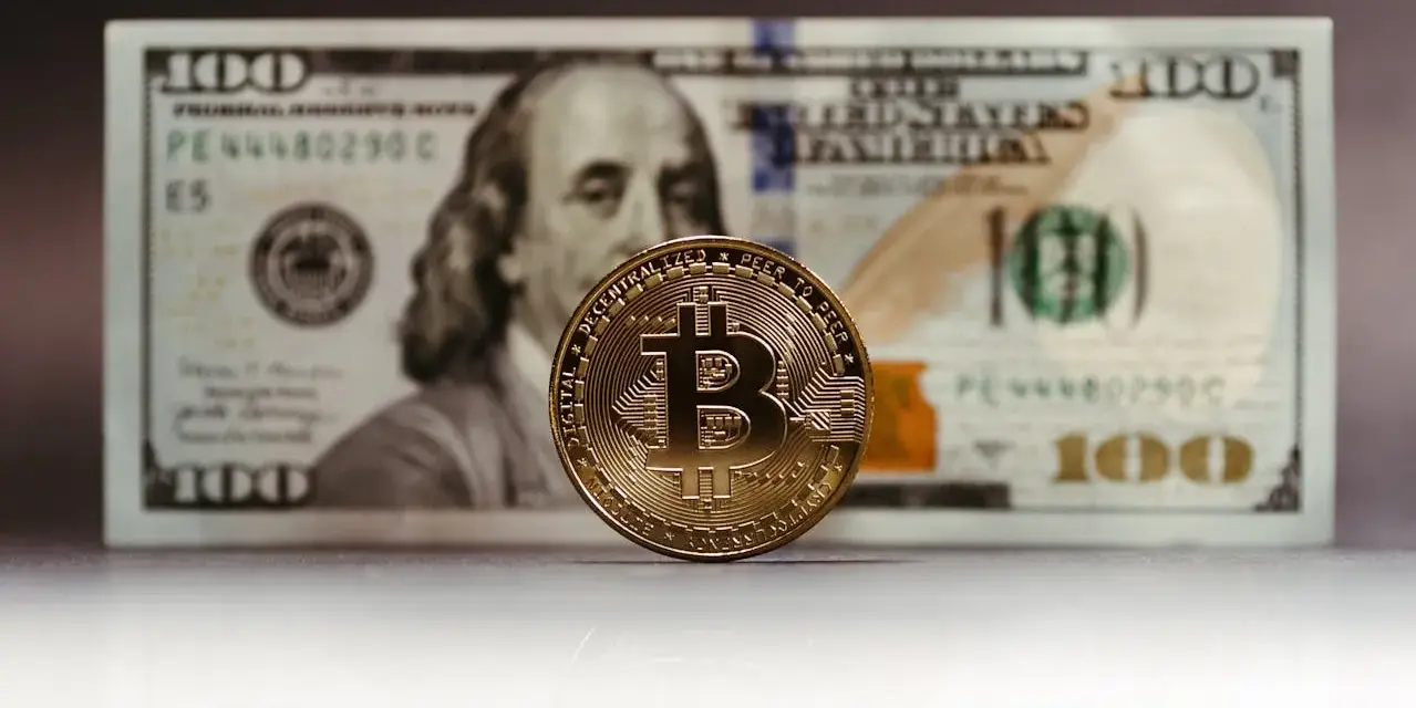 Złoty Bitcoin na tle banknotu 100 dolarów. Zastanawiasz się, jak rozliczyć podatek od zysku z kryptowalut?