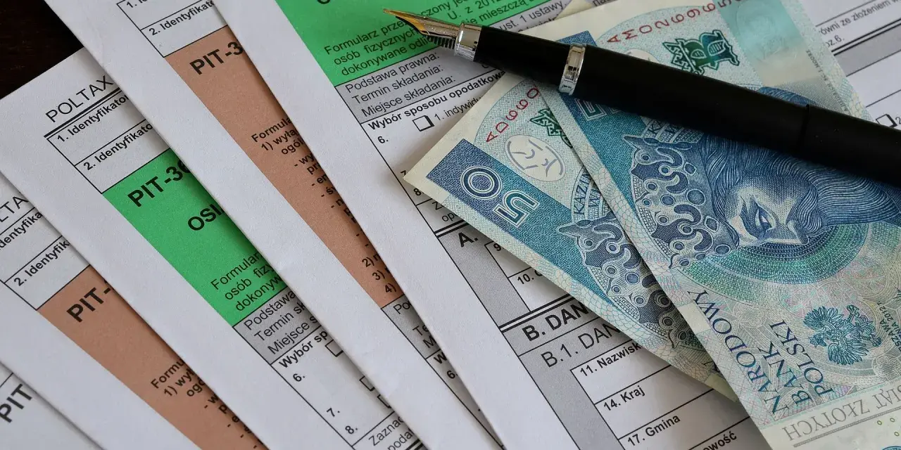 Formularze PIT, długopis i polskie banknoty. Miesięczna kwota wolna od podatku jest ważnym elementem rozliczeń.