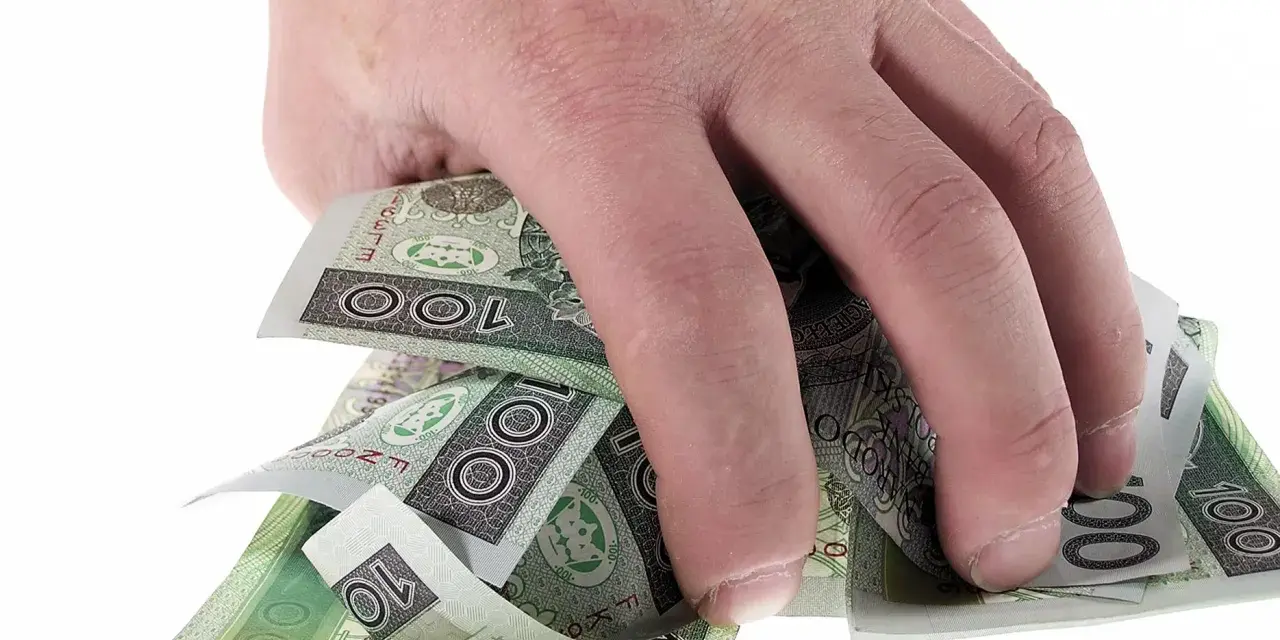 Dłoń trzyma plik polskich banknotów 100 zł. Może to symbolizować zwrot refinansowania lub po prostu oszczędności.