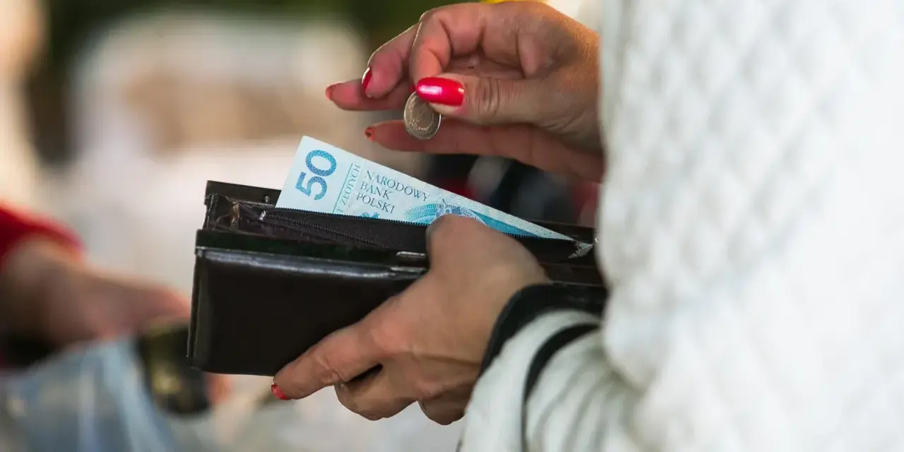 Kobieta z czerwonymi paznokciami wkłada monetę do portfela z banknotem 50 zł. Lekcja jak nie wydawać pieniędzy.