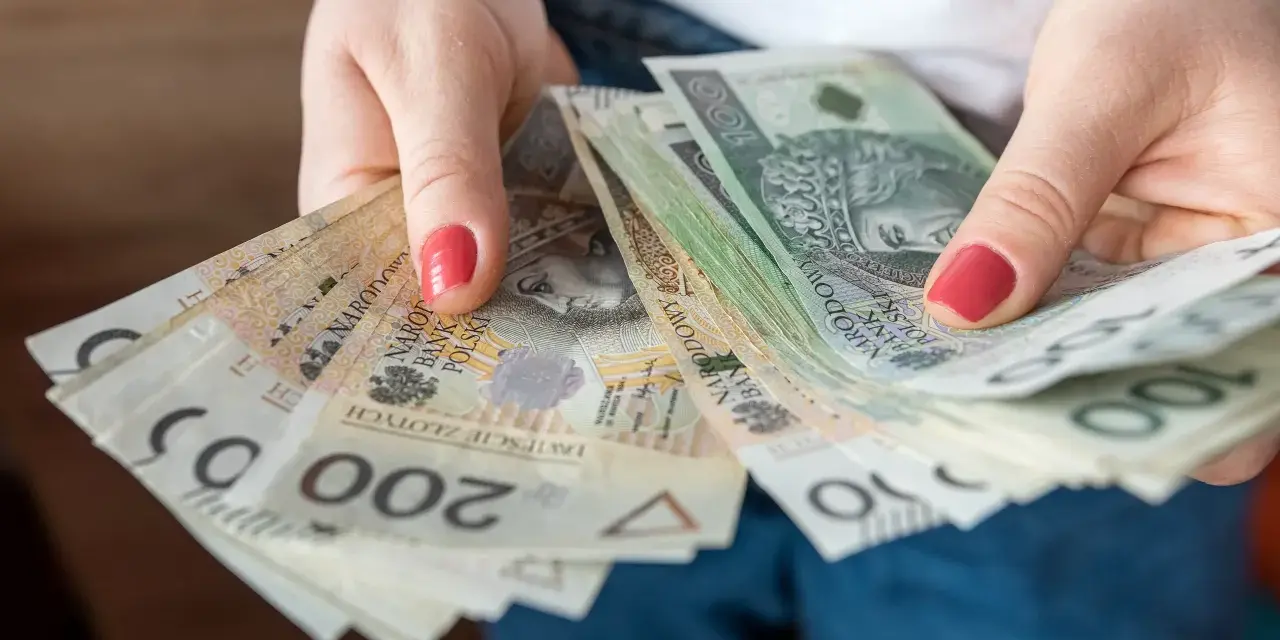 Dłonie trzymają stos banknotów 100 i 200 zł. To może być kwota wolna od podatku 60000 zł, która pozwala na swobodne planowanie wydatków.