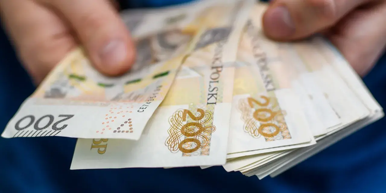 Dłonie trzymają stos banknotów 200 zł. To symbol oszczędności Polaków, które budują bezpieczeństwo finansowe.