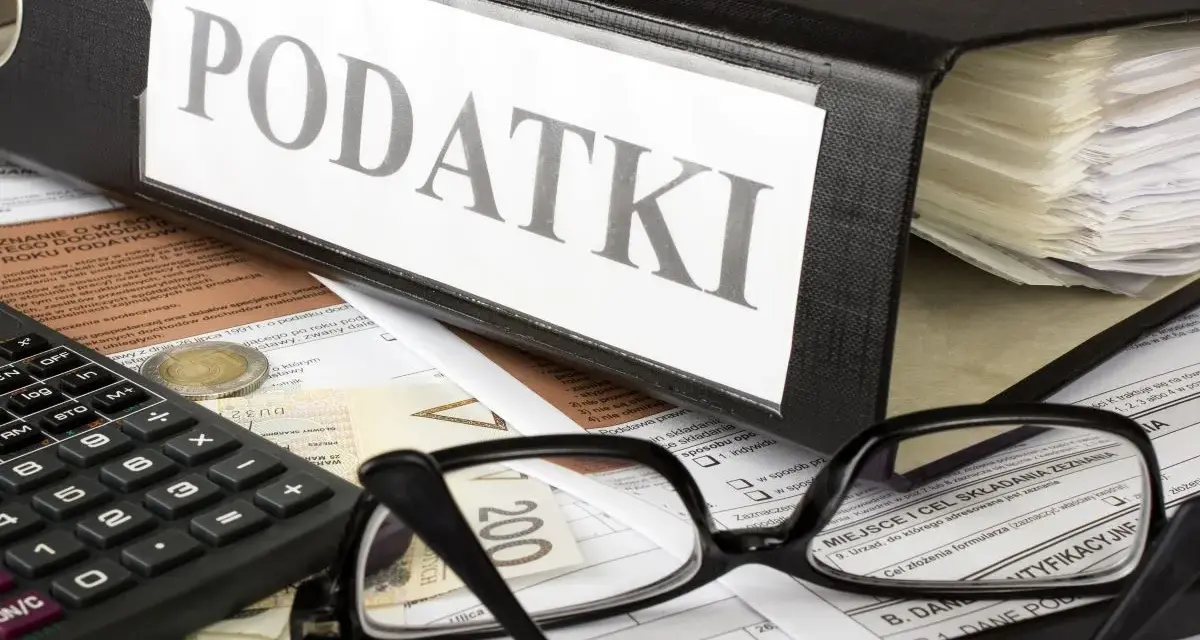 Segregator z napisem "PODATKI", kalkulator, okulary i dokumenty. Tabela kwota wolna od podatku 30 tys. jest częścią tych dokumentów.