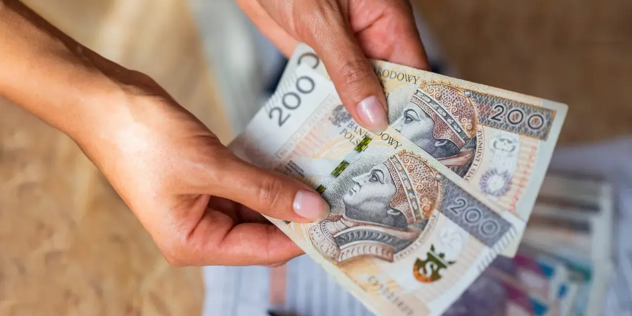 Dłonie trzymają banknoty 200 zł. Czy na lokatę można wpłacać pieniądze co miesiąc?