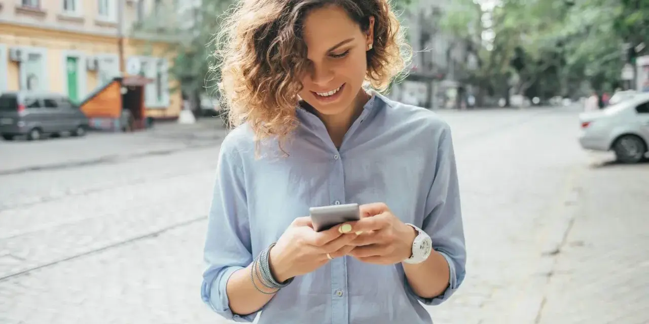 Uśmiechnięta kobieta na ulicy sprawdza telefon, być może szuka informacji o pożyczka kontomatik.
