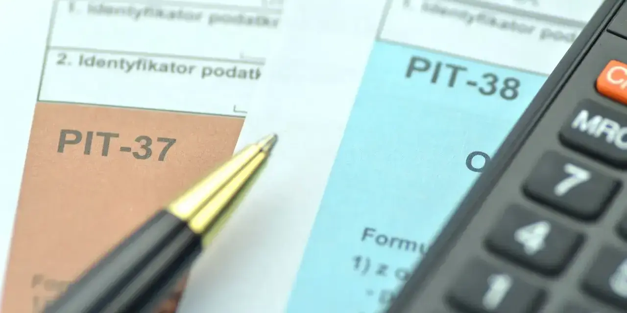 Dwa formularze podatkowe, PIT-38 i PIT-37, leżą obok siebie, gotowe do wypełnienia. Obok leży długopis i kalkulator.