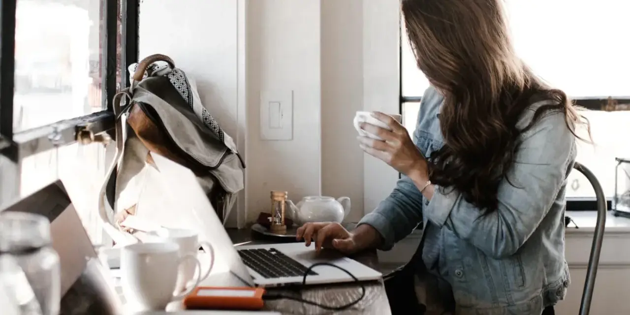Kobieta pracuje przy laptopie, pijąc kawę. To idealne miejsce do rozwijania swoich freelancer zarobki.