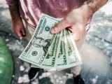 Dłoń trzyma kilka banknotów po 20 dolarów, symbolizując sposób, jak zarabiać więcej.