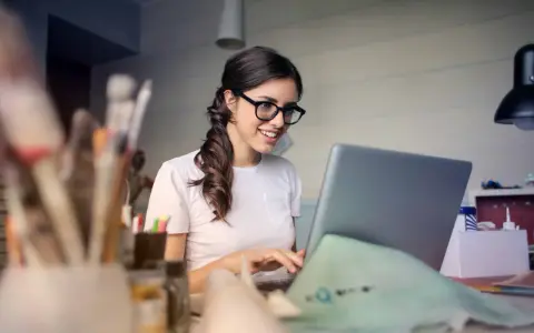 Uśmiechnięta kobieta w okularach pracuje przy laptopie, realizując swoją pracę dodatkową z domu.