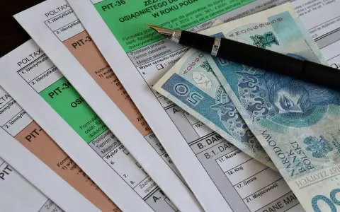 Formularze PIT, długopis i polskie banknoty. Miesięczna kwota wolna od podatku jest ważnym elementem rozliczeń.