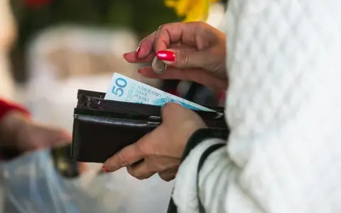 Kobieta z czerwonymi paznokciami wkłada monetę do portfela z banknotem 50 zł. Lekcja jak nie wydawać pieniędzy.