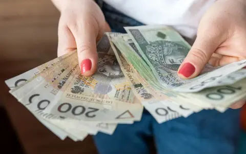 Dłonie trzymają stos banknotów 100 i 200 zł. To może być kwota wolna od podatku 60000 zł, która pozwala na swobodne planowanie wydatków.