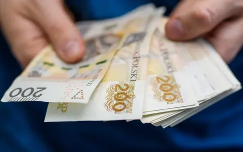 Dłonie trzymają stos banknotów 200 zł. To symbol oszczędności Polaków, które budują bezpieczeństwo finansowe.