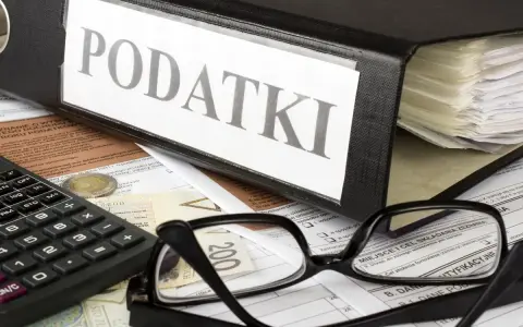 Segregator z napisem "PODATKI", kalkulator, okulary i dokumenty. Tabela kwota wolna od podatku 30 tys. jest częścią tych dokumentów.