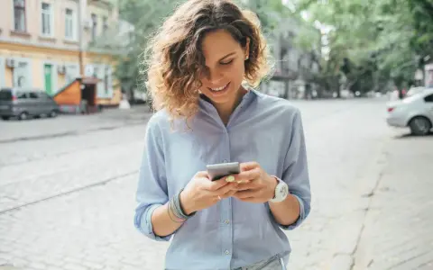 Uśmiechnięta kobieta na ulicy sprawdza telefon, być może szuka informacji o pożyczka kontomatik.