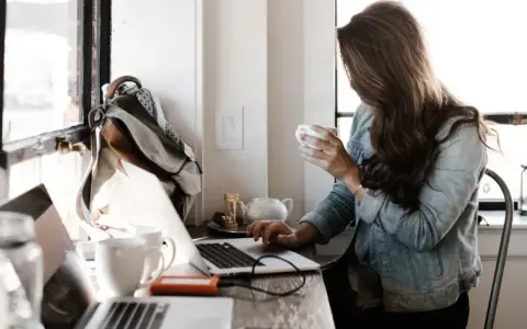 Kobieta pracuje przy laptopie, pijąc kawę. To idealne miejsce do rozwijania swoich freelancer zarobki.
