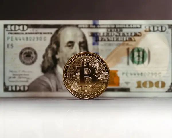 Złoty Bitcoin na tle banknotu 100 dolarów. Zastanawiasz się, jak rozliczyć podatek od zysku z kryptowalut?