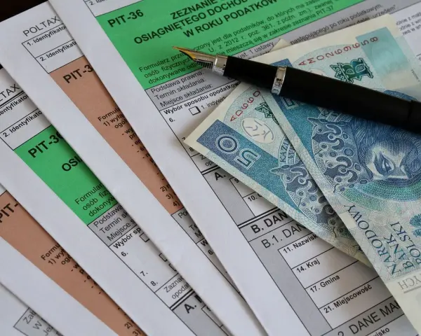 Formularze PIT, długopis i polskie banknoty. Miesięczna kwota wolna od podatku jest ważnym elementem rozliczeń.