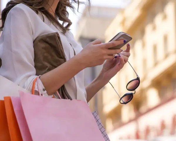 Kobieta z zakupami sprawdza telefon, planując refinansowanie pożyczki.