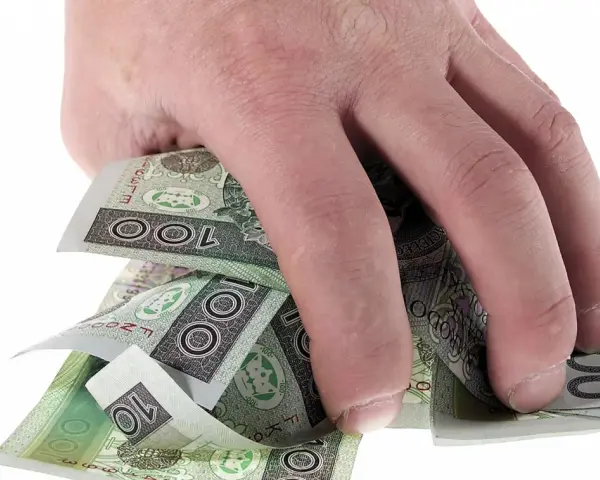 Dłoń trzyma plik polskich banknotów 100 zł. Może to symbolizować zwrot refinansowania lub po prostu oszczędności.