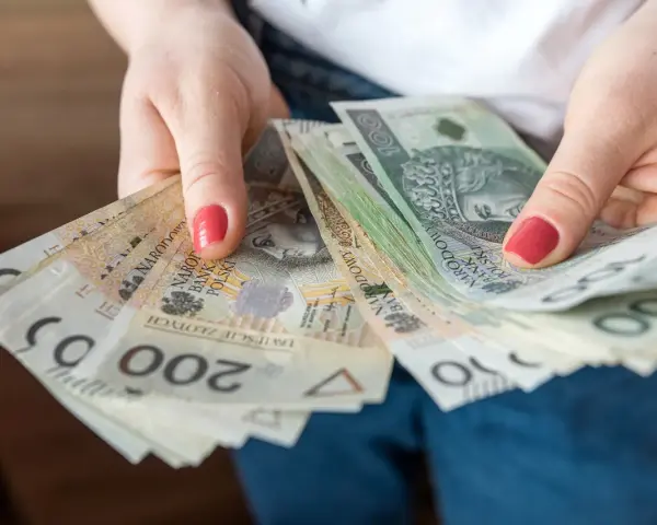 Dłonie trzymają stos banknotów 100 i 200 zł. To może być kwota wolna od podatku 60000 zł, która pozwala na swobodne planowanie wydatków.
