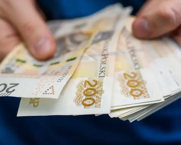 Dłonie trzymają stos banknotów 200 zł. To symbol oszczędności Polaków, które budują bezpieczeństwo finansowe.