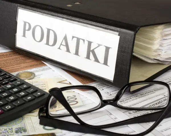 Segregator z napisem "PODATKI", kalkulator, okulary i dokumenty. Tabela kwota wolna od podatku 30 tys. jest częścią tych dokumentów.