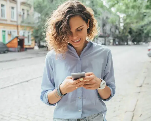Uśmiechnięta kobieta na ulicy sprawdza telefon, być może szuka informacji o pożyczka kontomatik.