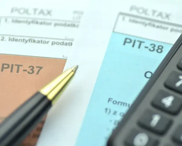 Dwa formularze podatkowe, PIT-38 i PIT-37, leżą obok siebie, gotowe do wypełnienia. Obok leży długopis i kalkulator.