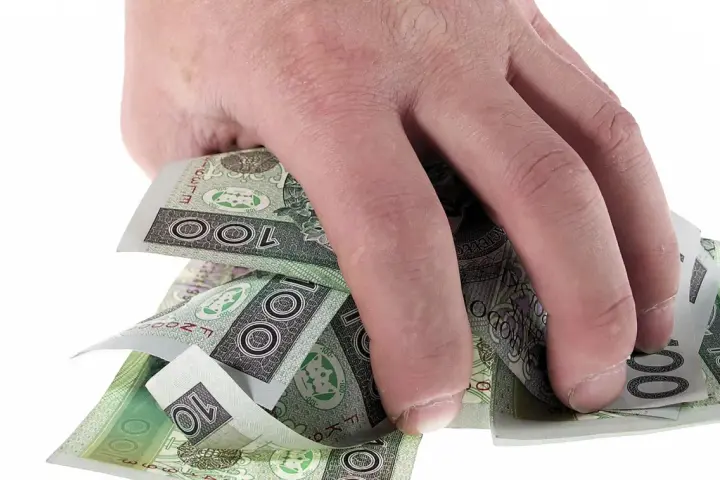 Dłoń trzyma plik polskich banknotów 100 zł. Może to symbolizować zwrot refinansowania lub po prostu oszczędności.