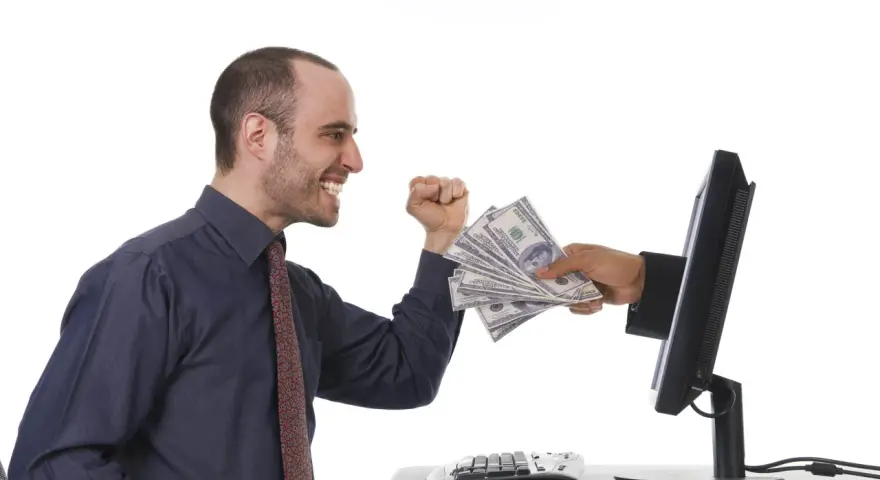 Uśmiechnięty mężczyzna otrzymuje stos banknotów z ekranu komputera. To symbol zarabiania na klikaniu.