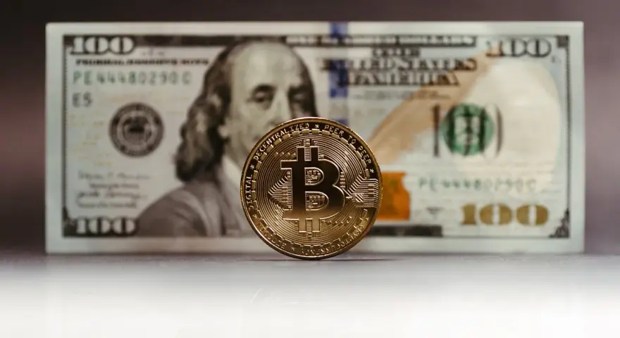 Złoty Bitcoin na tle banknotu 100 dolarów. Zastanawiasz się, jak rozliczyć podatek od zysku z kryptowalut?