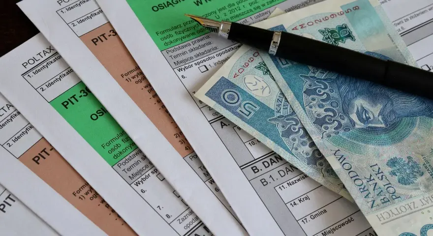 Formularze PIT, długopis i polskie banknoty. Miesięczna kwota wolna od podatku jest ważnym elementem rozliczeń.