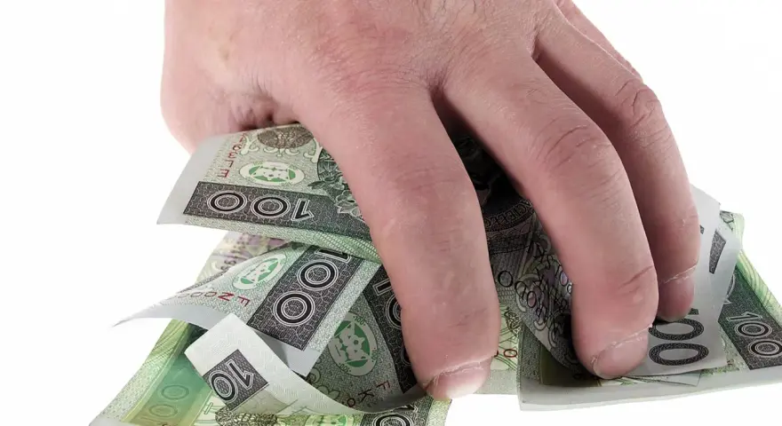 Dłoń trzyma plik polskich banknotów 100 zł. Może to symbolizować zwrot refinansowania lub po prostu oszczędności.