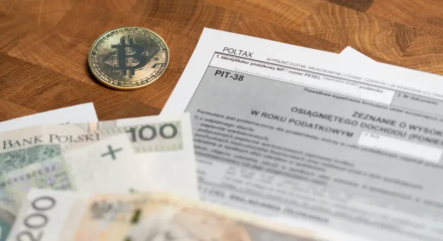 Złoty bitcoin obok formularza PIT-38 i polskich banknotów. Może to oznaczać niedopłatę podatku 3 zł.