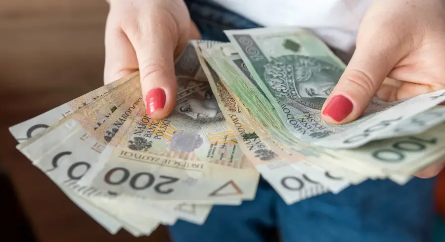 Dłonie trzymają stos banknotów 100 i 200 zł. To może być kwota wolna od podatku 60000 zł, która pozwala na swobodne planowanie wydatków.
