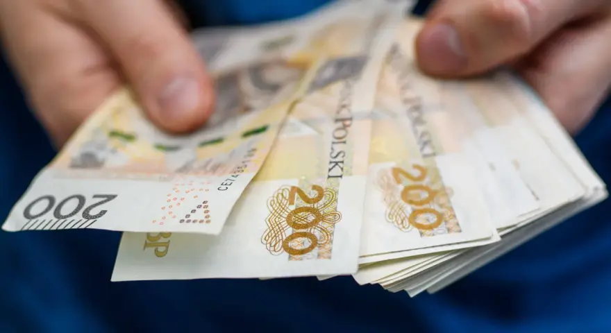 Dłonie trzymają stos banknotów 200 zł. To symbol oszczędności Polaków, które budują bezpieczeństwo finansowe.