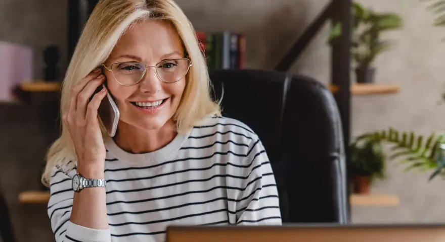 Uśmiechnięta kobieta w okularach rozmawia przez telefon, omawiając pożyczkę do domu klienta.
