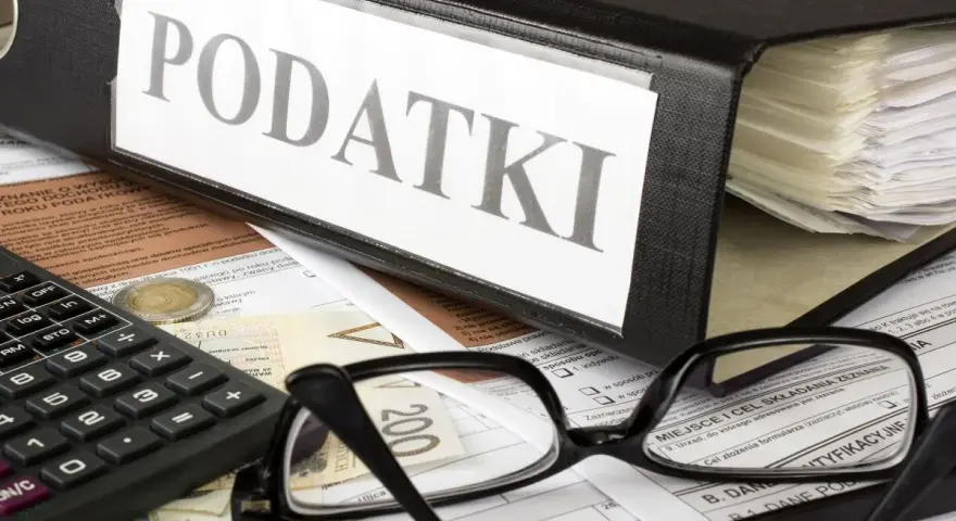Segregator z napisem "PODATKI", kalkulator, okulary i dokumenty. Tabela kwota wolna od podatku 30 tys. jest częścią tych dokumentów.
