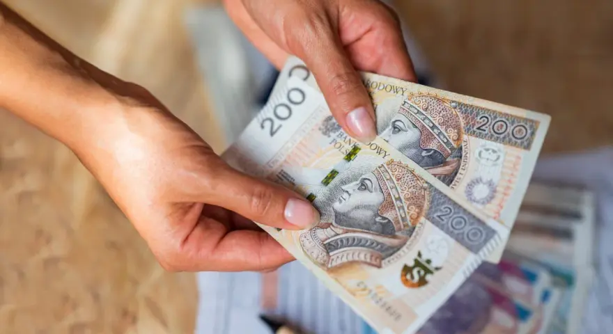 Dłonie trzymają banknoty 200 zł. Czy na lokatę można wpłacać pieniądze co miesiąc?