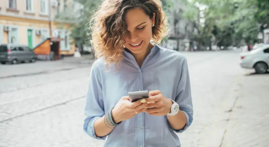 Uśmiechnięta kobieta na ulicy sprawdza telefon, być może szuka informacji o pożyczka kontomatik.